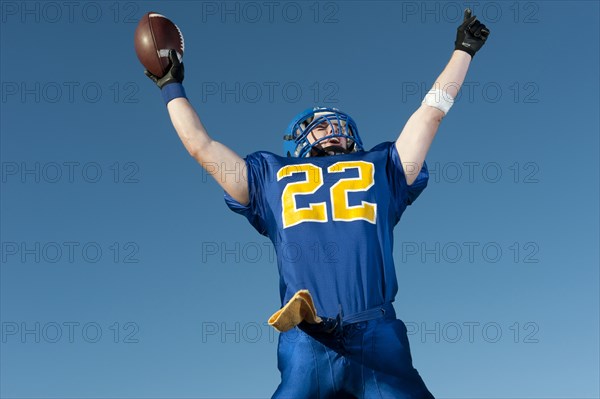 Caucasian football player holding football with arms raised
