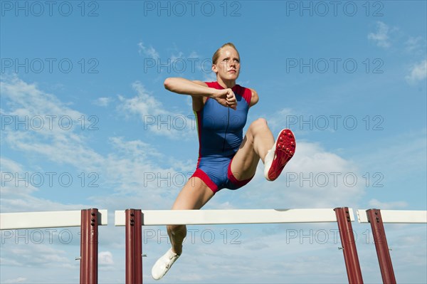 Caucasian runner jumping over hurdles on track