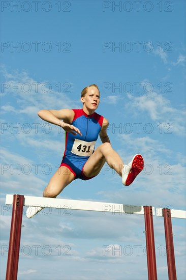 Caucasian runner jumping over hurdles on track