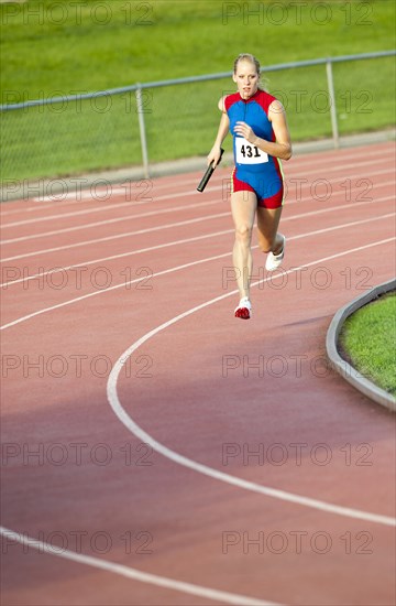 Caucasian runner holding baton running on track