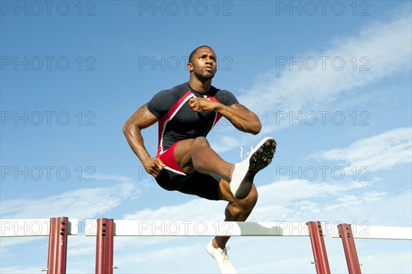 Black runner jumping hurdles in track race