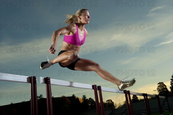 Caucasian runner jumping over hurdles