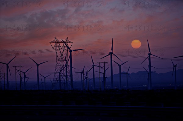 Silhouette of wind turbines and power lines at sunset