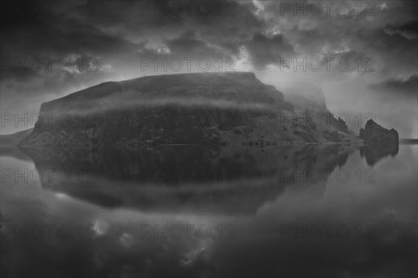 Snowy mountain under cloudy sky reflected in lake