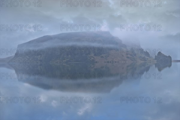 Snowy mountain under cloudy sky reflected in lake