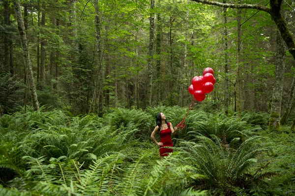 Korean woman holding red balloons in lush forest