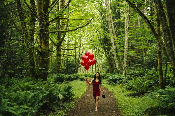 Korean woman holding red balloons in lush forest