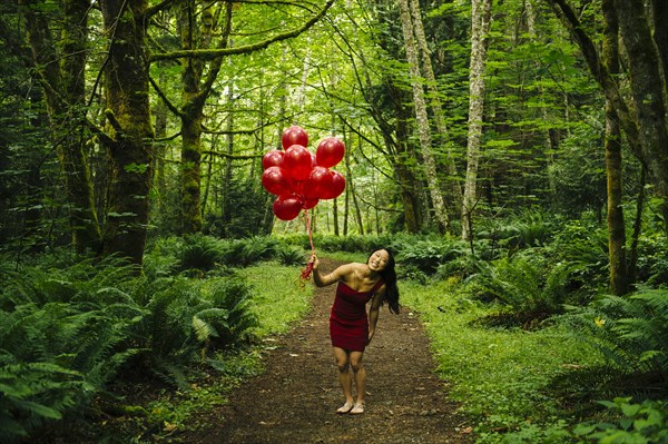 Korean woman holding red balloons in lush forest