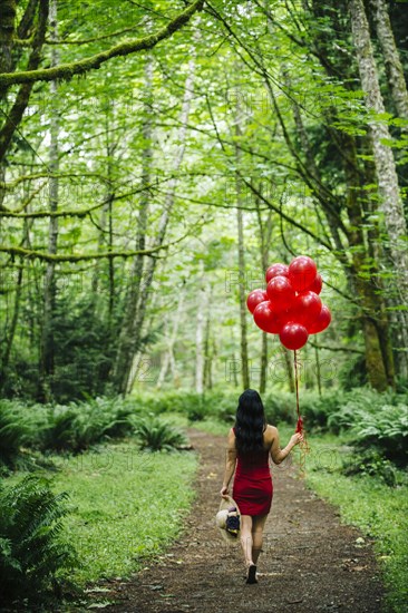 Korean woman holding red balloons in lush forest