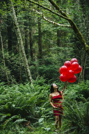 Korean woman holding red balloons in lush forest