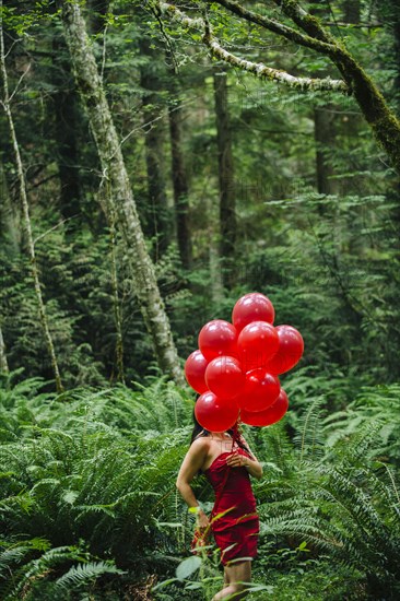 Korean woman holding red balloons in lush forest