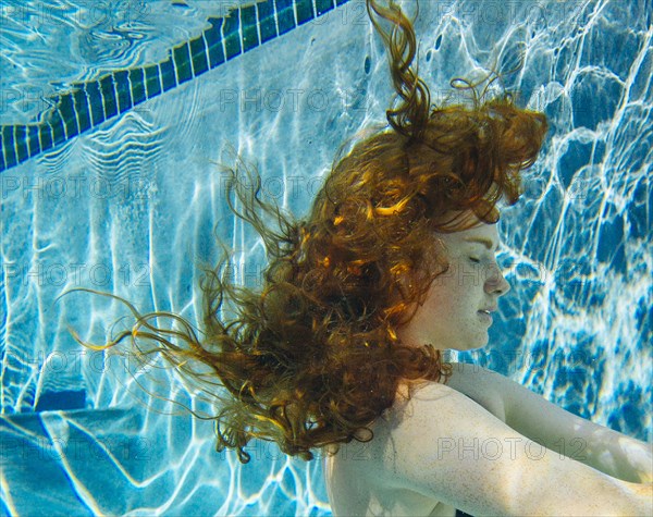 Teenage girl with red hair swimming underwater in pool