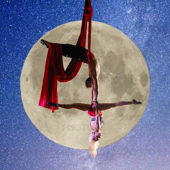 Caucasian acrobats performing with silk ropes by full moon