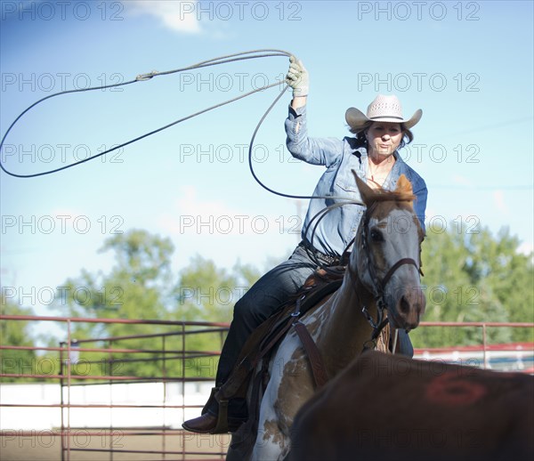 Caucasian cowgirl on horse throwing lasso on ranch