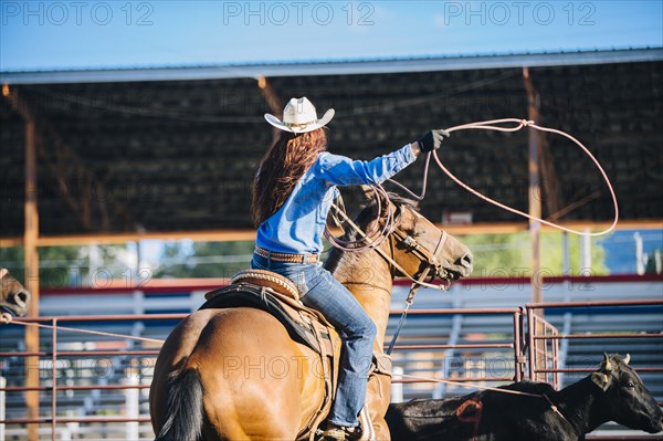 Caucasian cowgirl on horse throwing lasso in rodeo on ranch