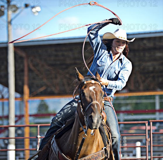 Caucasian cowgirl on horse throwing lasso in rodeo on ranch