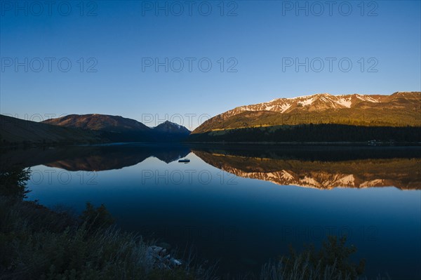 Remote mountains and blue sky reflected in still lake