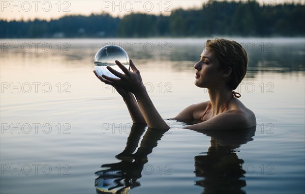 Caucasian woman holding crystal ball in still lake