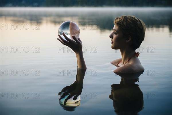 Caucasian woman holding crystal ball in still lake