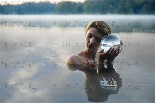 Caucasian woman holding crystal ball in still lake