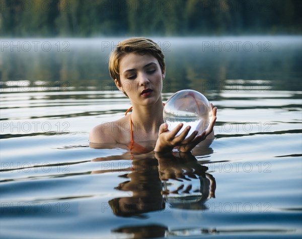 Caucasian woman holding crystal ball in still lake