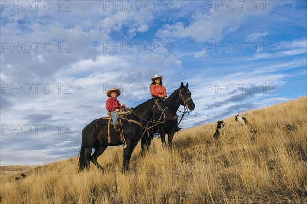 Caucasian mother and son on horseback on grassy hill