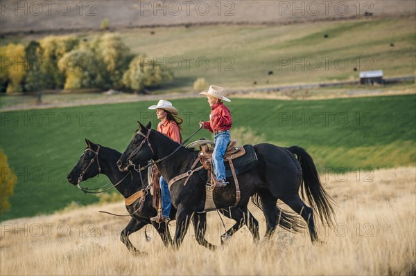 Caucasian mother and son riding horses in grassy field