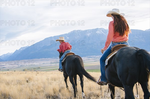 Caucasian mother and son riding horses in grassy field