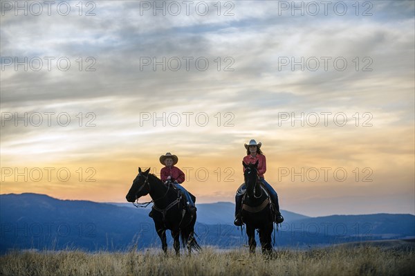 Caucasian mother and son riding horses in grassy field