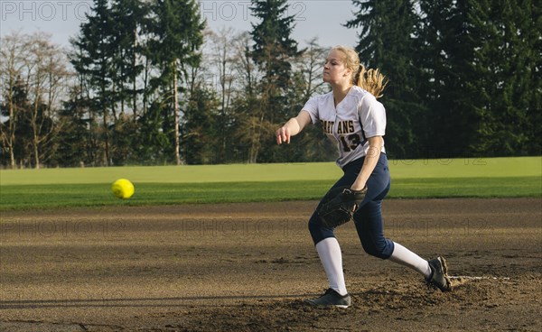 Caucasian softball player pitching ball in field