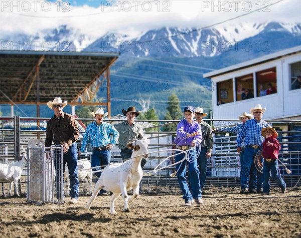 Cowboys watching boy throw lasso in rodeo