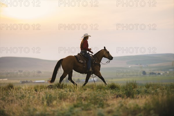 Caucasian cowgirl riding horse in rural field