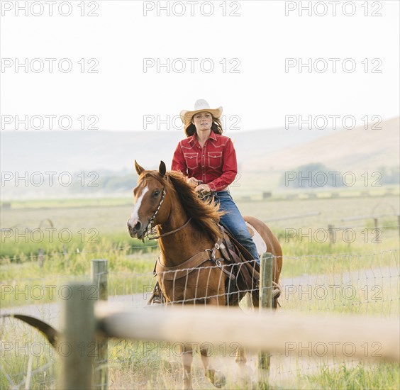 Caucasian cowgirl riding horse on ranch
