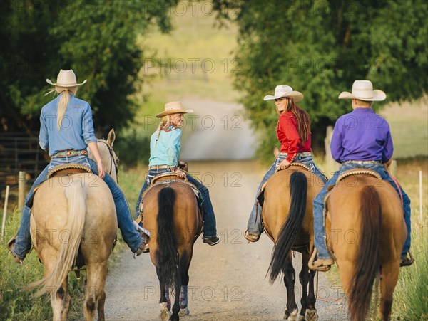 Cowgirls and cowboy riding horses in rural road