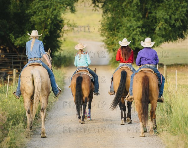 Cowgirls and cowboy riding horses in rural road