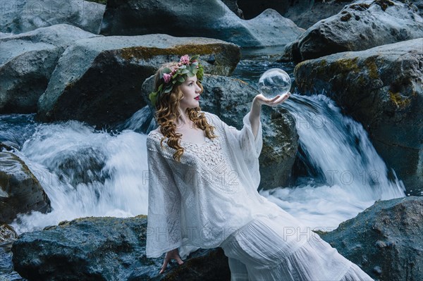Caucasian woman holding crystal ball at river waterfall