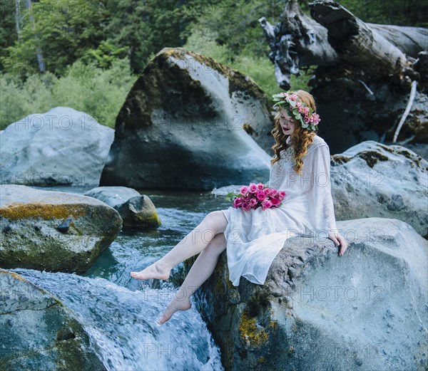Caucasian woman wearing flower crown on rock at river waterfall