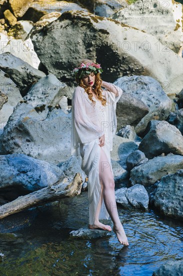 Caucasian woman wearing flower crown dipping toe in river