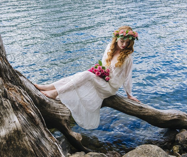 Caucasian woman wearing flower crown on log at river