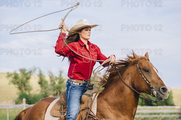 Caucasian cowgirl throwing lasso on horseback