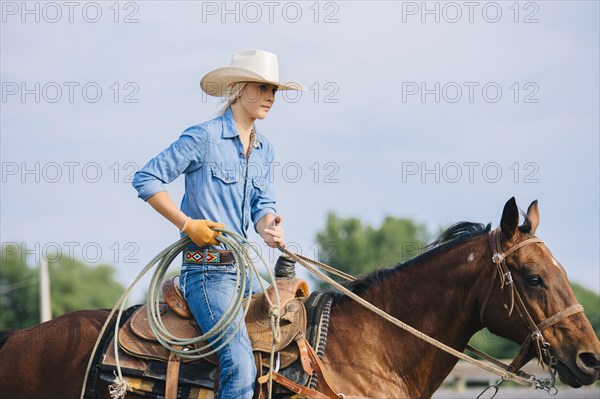 Caucasian cowgirl holding lasso on horseback