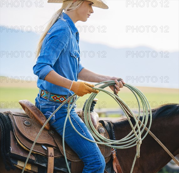 Caucasian cowgirl holding lasso on horseback