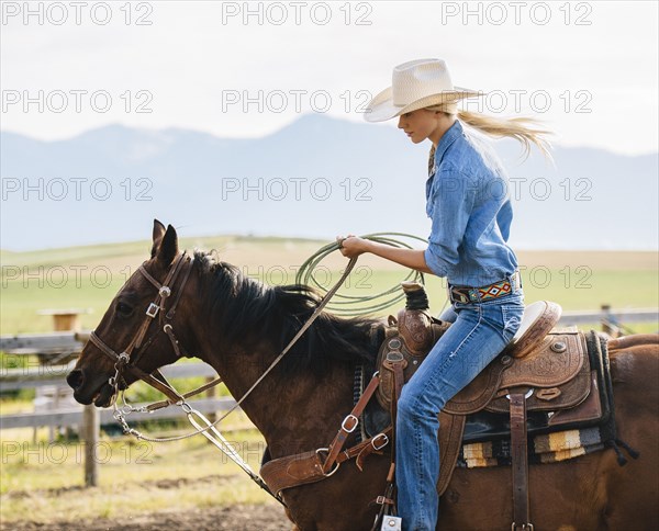 Caucasian cowgirl holding lasso on horseback