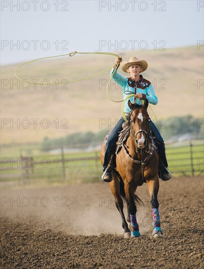 Caucasian cowgirl throwing lasso on horseback