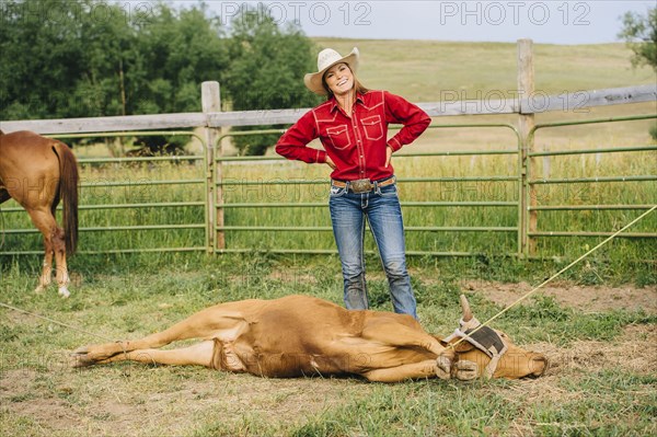 Caucasian cowgirl smiling with tied cattle on ranch