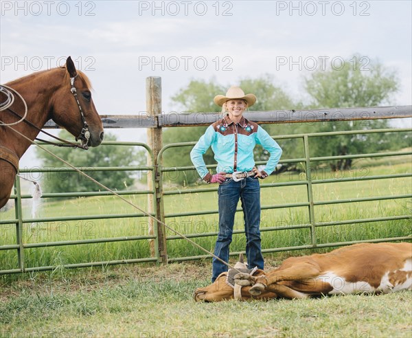 Cowgirl smiling with tied cattle on ranch