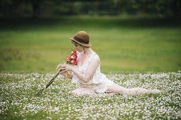 Caucasian woman sitting in field of flowers smelling roses