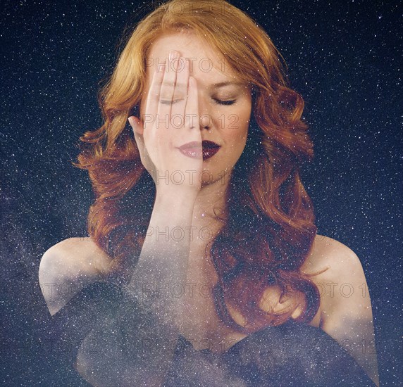 Multiple exposure of Caucasian woman with hand on face in starry sky