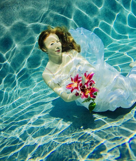 Caucasian woman wearing dress holding bouquet of flowers underwater