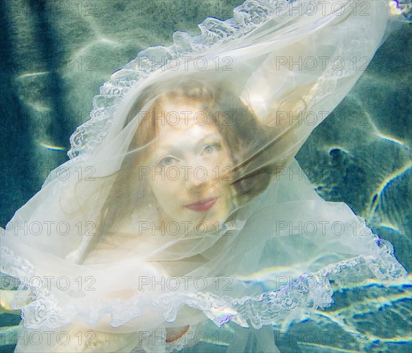 Caucasian woman wearing dress swimming underwater